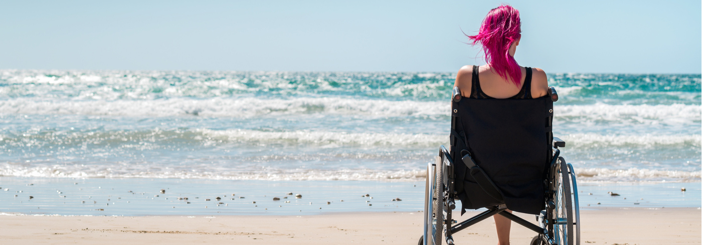 Woman in a wheelchair on the beach watching the ocean water.