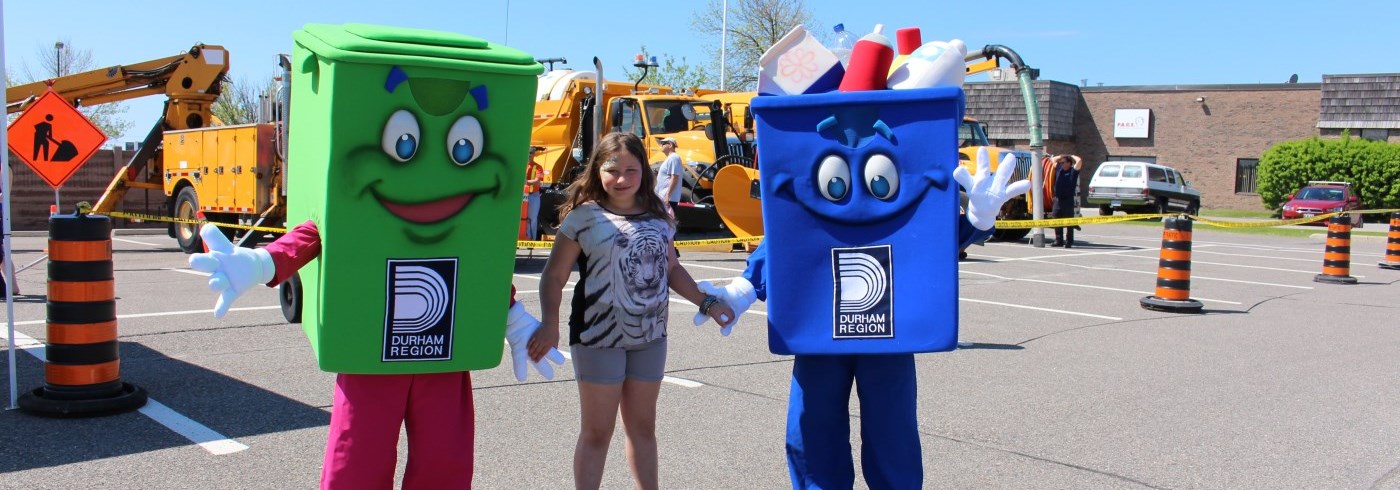Young girl holding hands with green bin and blue box mascots at event 