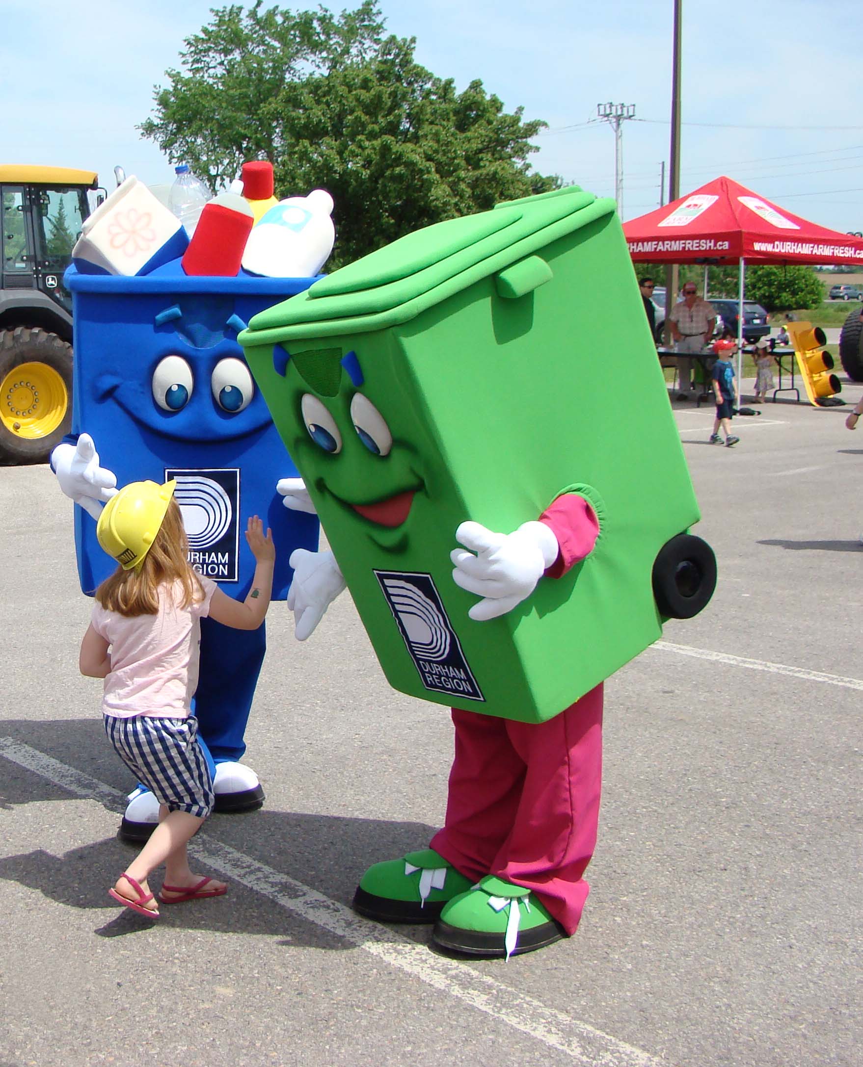 A photograph of a child with mascot recycling and green waste bins