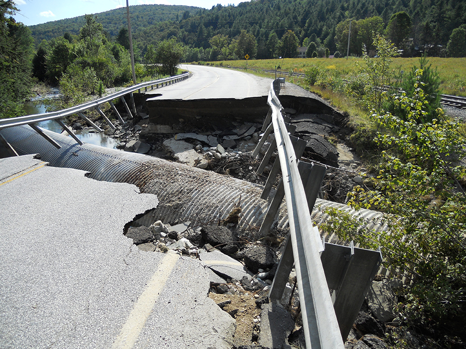A picture of a collapsed road in a rural setting with pipes exposed underneath