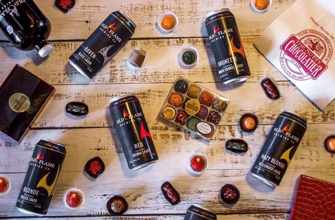 Old flame beer cans on a wooden table surrounded by Nutty Chocolatier chocolates