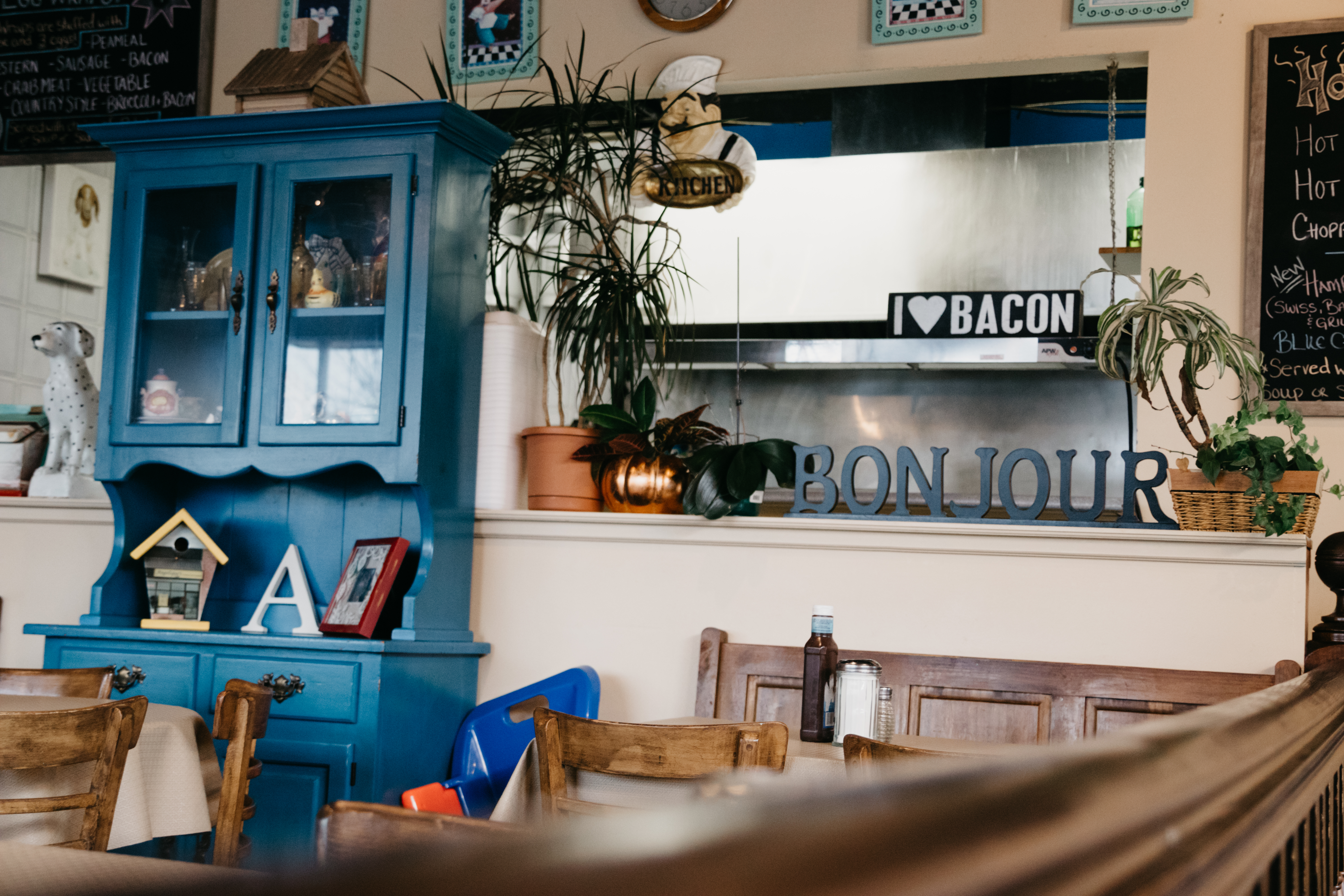 Wooden tables and chairs, bright blue cabinet and decor and kitchen area at Angeliques Family Restaurant.