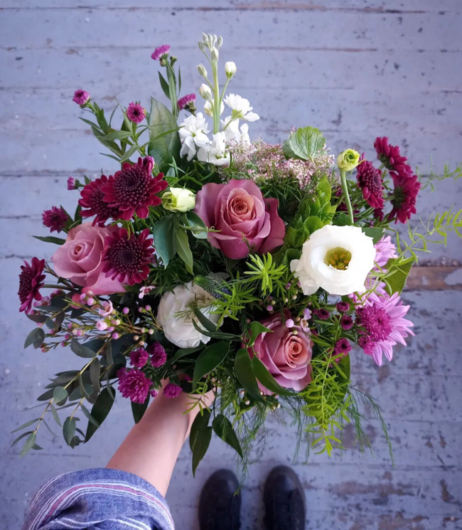 Hand holding a bouquet of pink, white and deep purple flowers