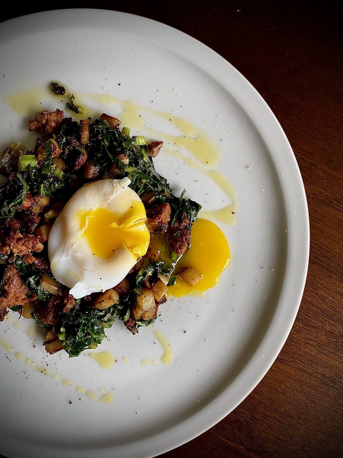 Poached duck egg with swiss chard and chorizo hash on a white plate