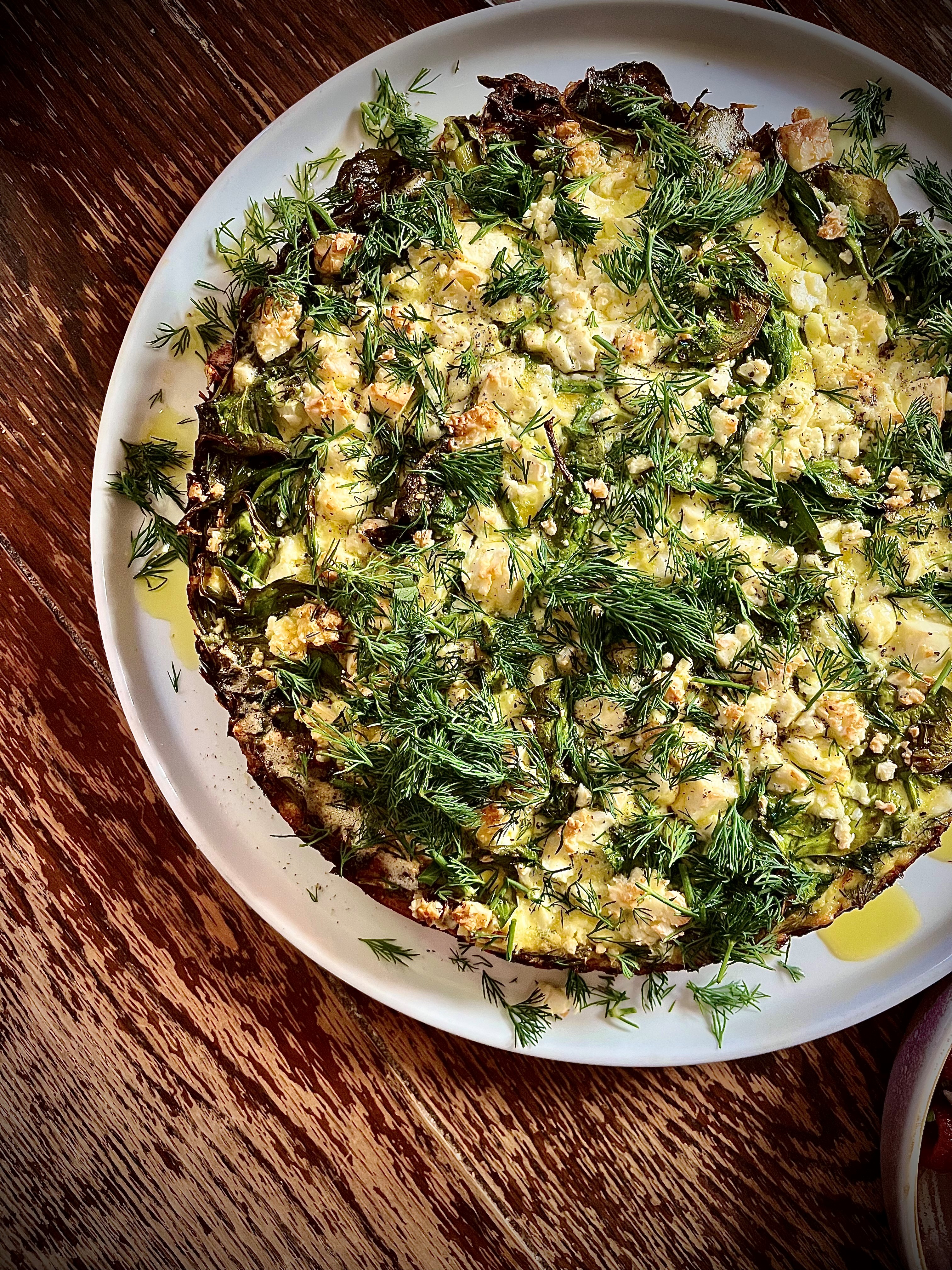 Duck egg and herb frittata with feta and olive oil on a white plate