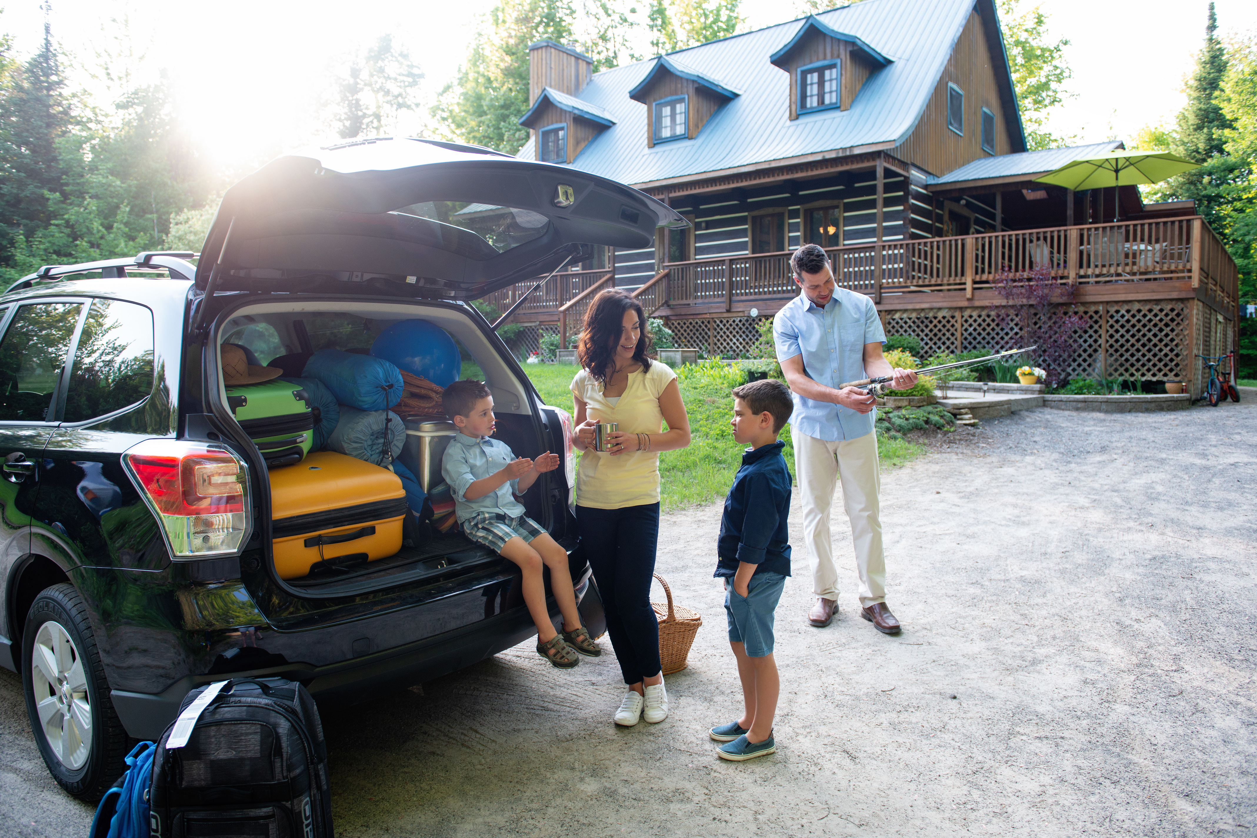 A family of four sitting getting ready for a road trip standing by their car