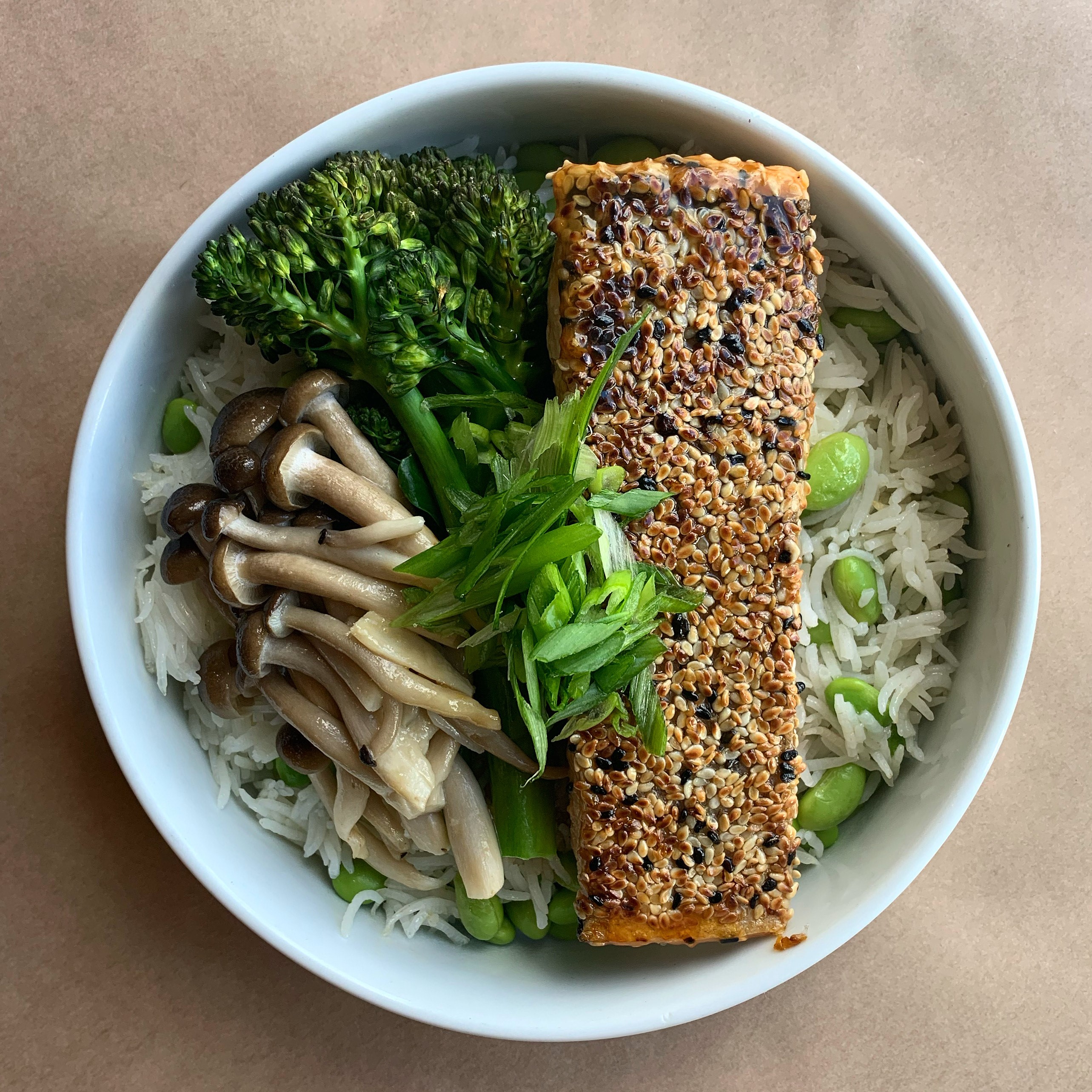 Plate of sesame crusted Atlantic salmon, house teriyaki sauce, shimeji mushrooms, broccolini, edamame, and rice.