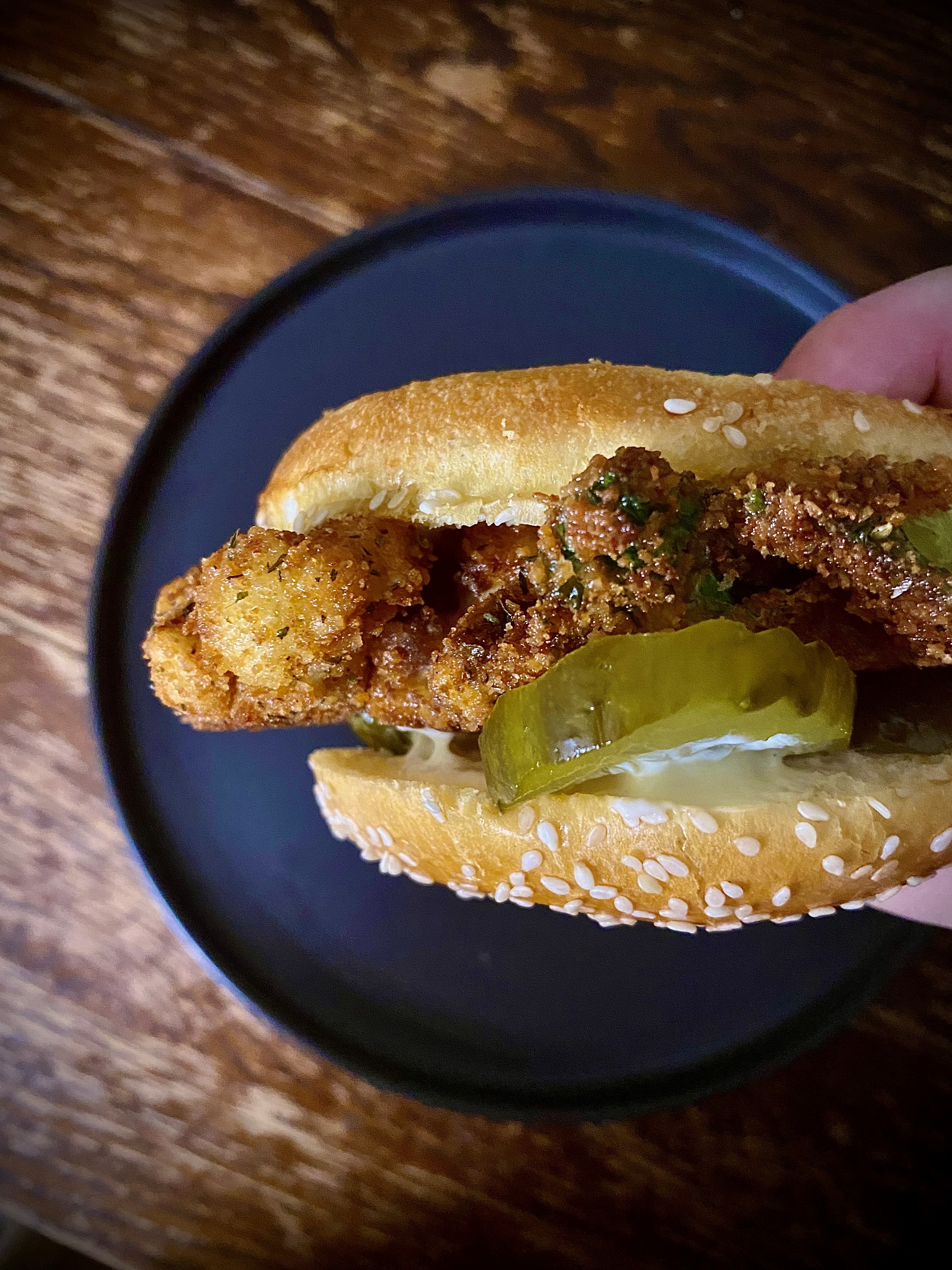 Hot Nashville cauliflower sandwich held in hand above blue plate