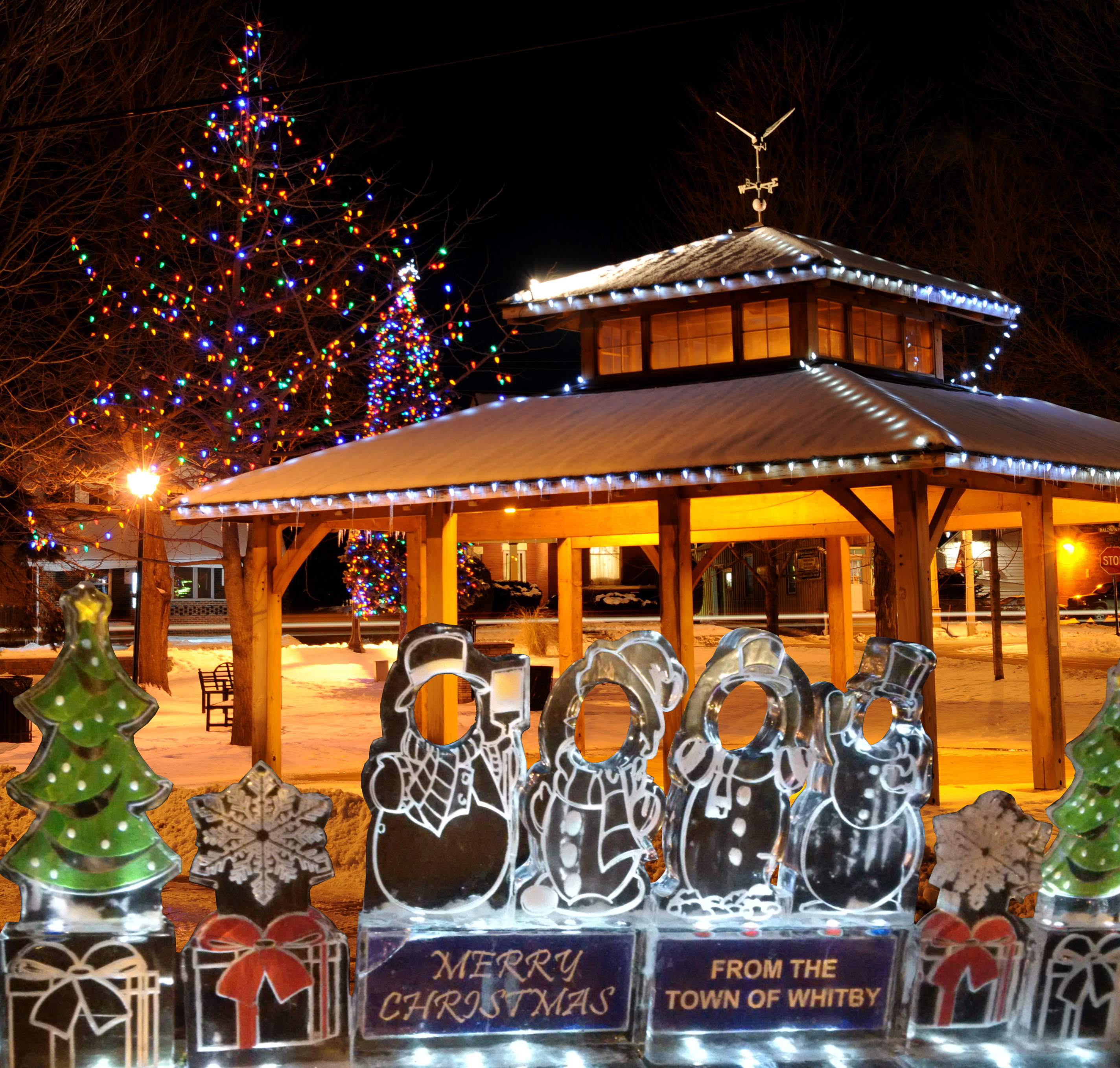 Image of gazebo and trees lit up in lights and snowman decoration that says Merry Christmas.