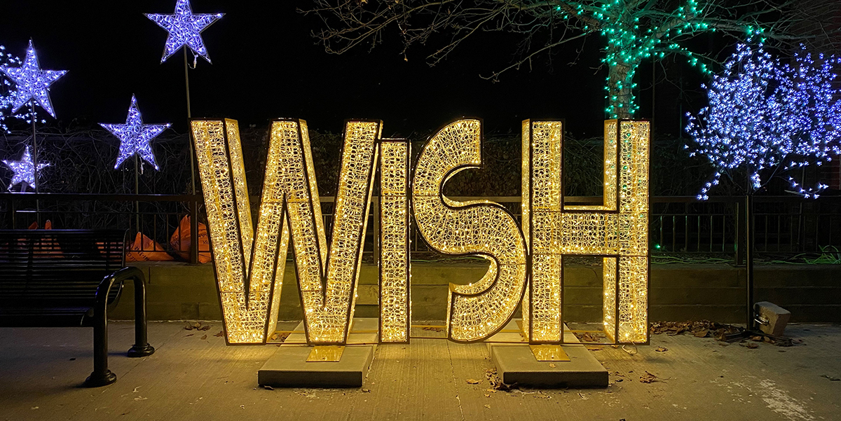 The word Wish light up in yellow lights surrounded by trees and stars lit with blue and green lights.