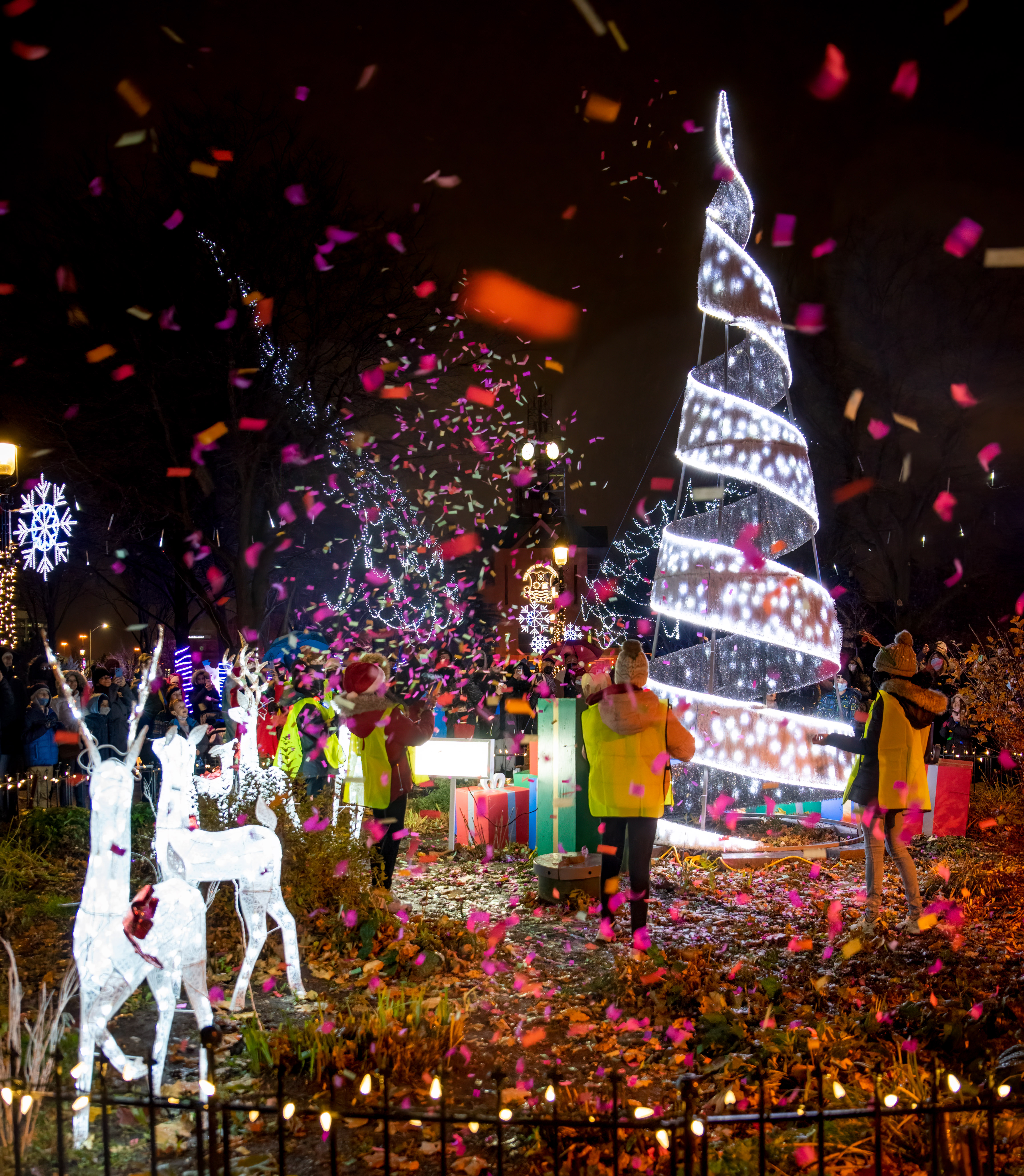 Image of holiday lights, confetti, children and decorations including a tree and deer statues.