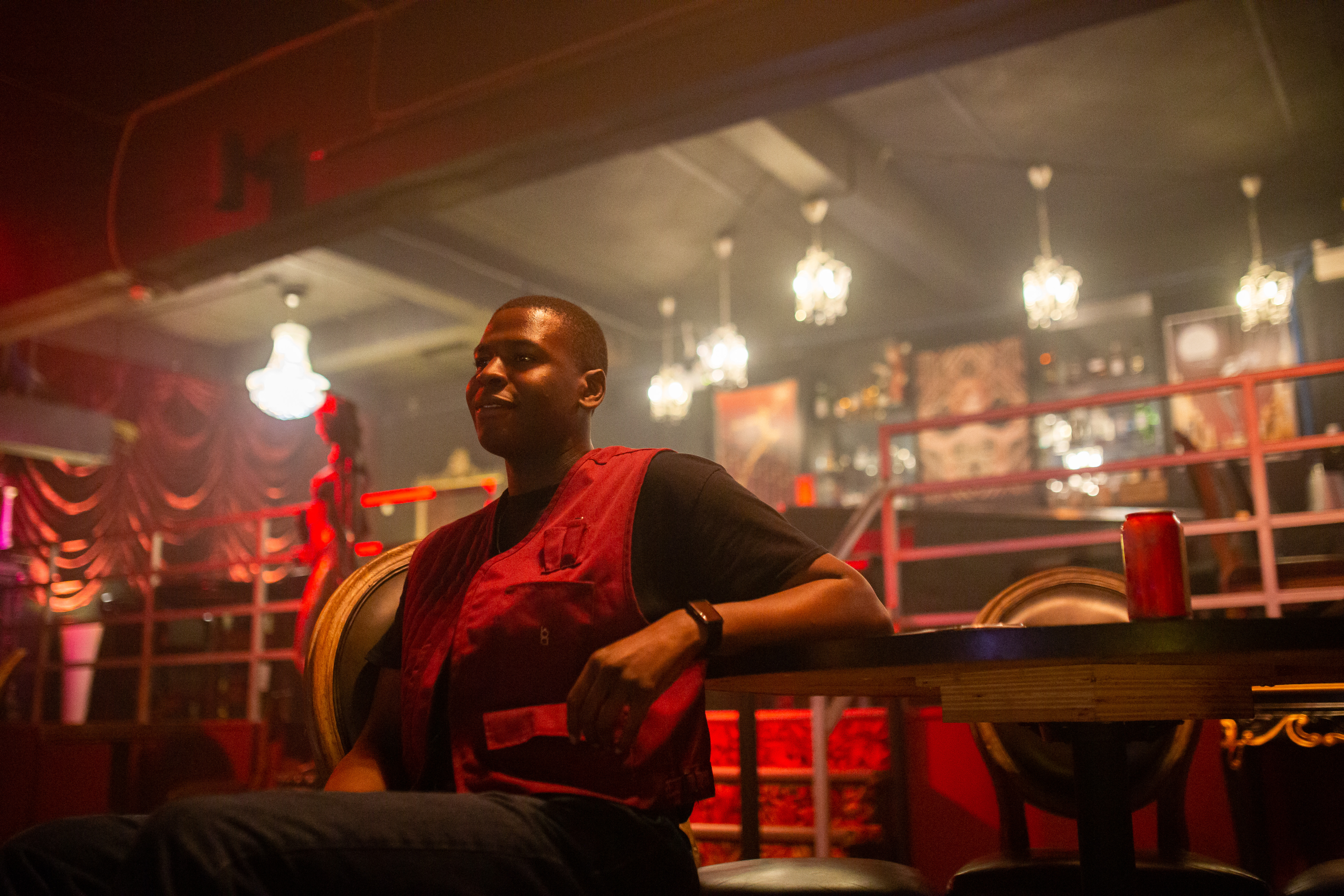 Man sitting at a bar wearing a red vest in moody lighting