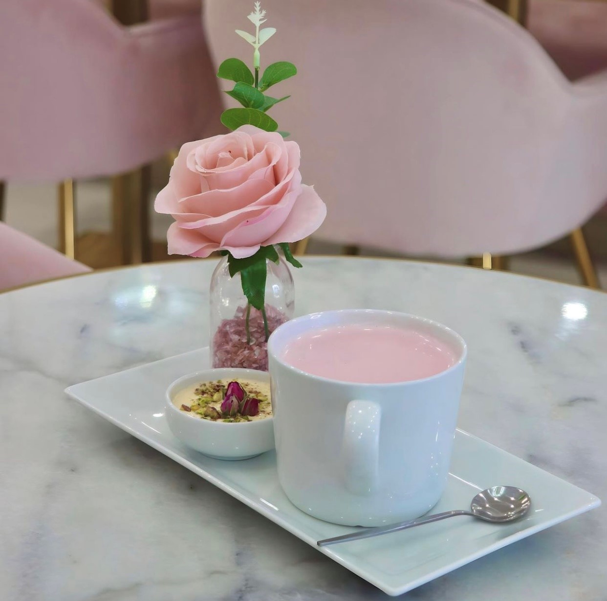 Pink tea in a white cup on a white tray with a pink flower and silver spoon