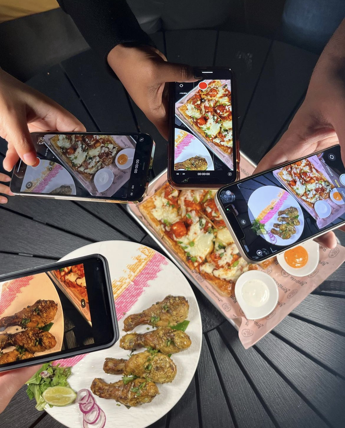 Four smart phones being held above plates of food to take a picture
