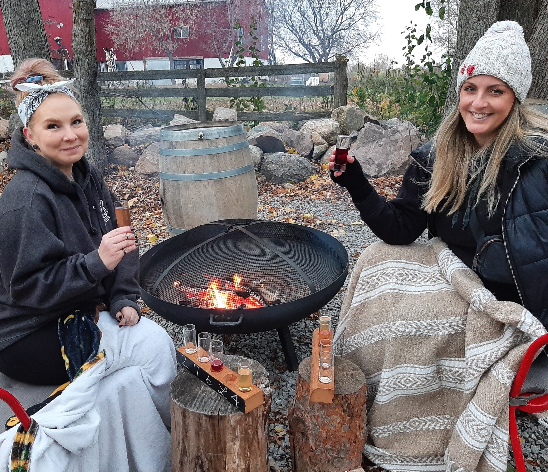 Two people sitting by a fire pit with blankets and a flight of Banjo cider