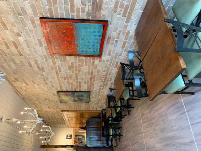 Tables along a brick wall with artwork inside Tin Restaurant in Uxbridge