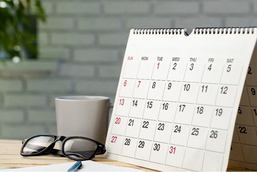 Paper calendar on a desk with a coffee cup and a pair of glasses