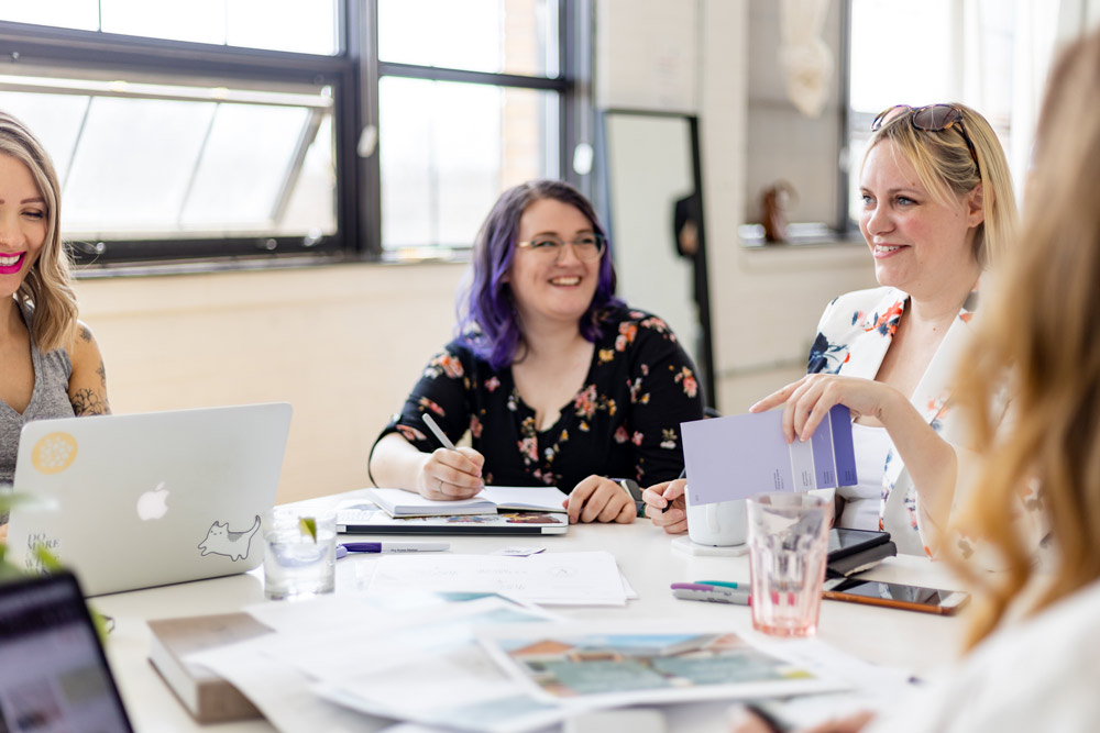 Staff at Brand Ambition working at a table together with smiles on their faces.