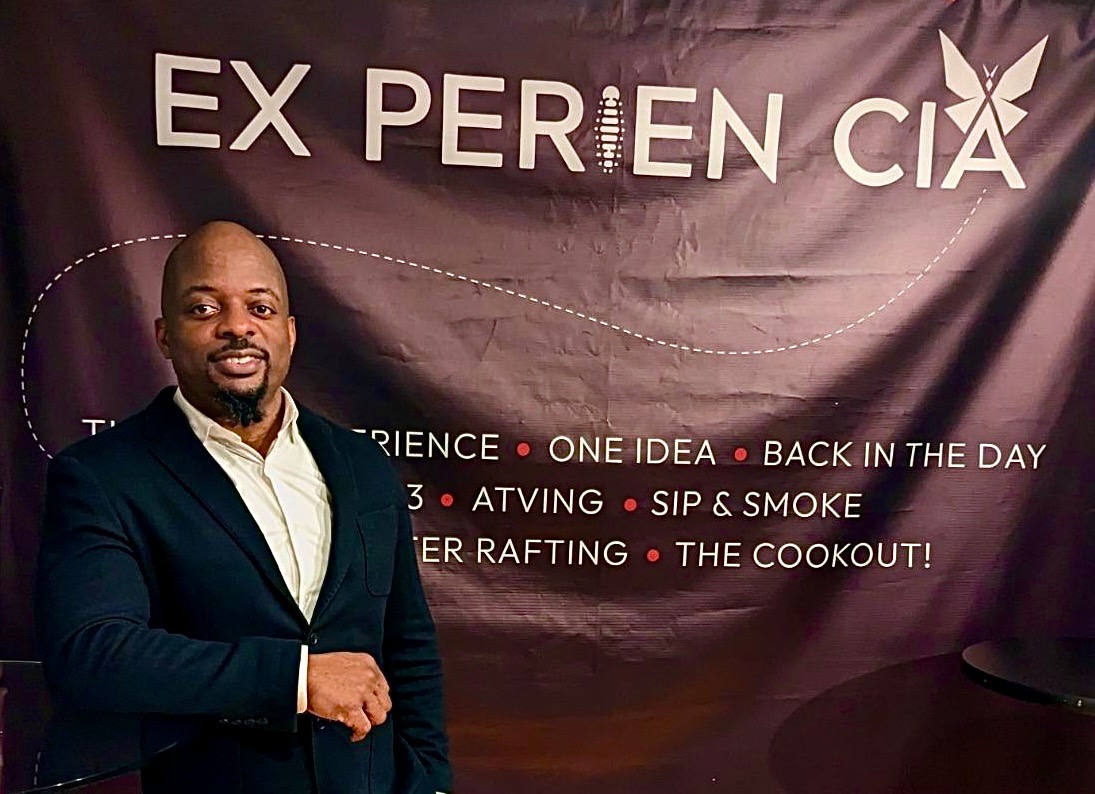 Brenton Alleyne, Entrepreneur, in front of a sign that reads, "Experiencia"