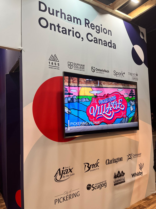 TV hanging in the Invest Durham booth with a Pickering Village mural on the screen.