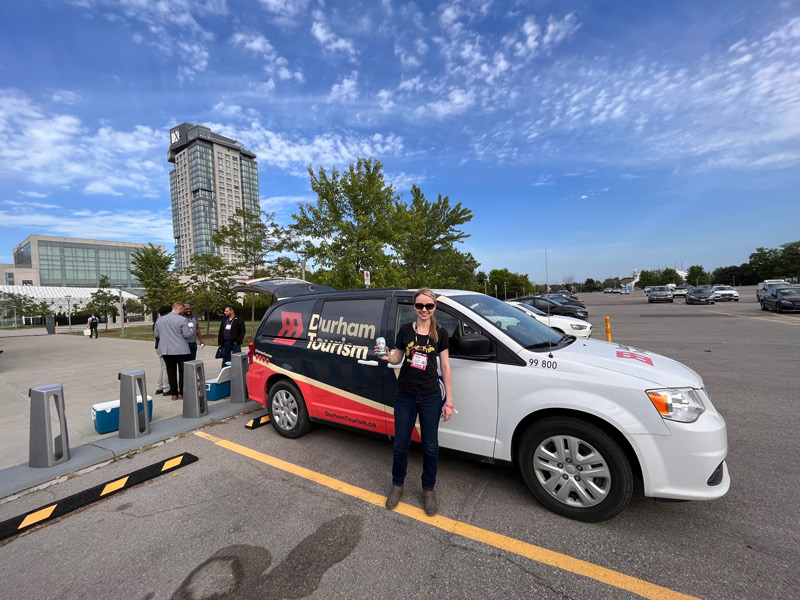 Invest Durham team member holding a can of Partake in front of the Durham Tourism van.