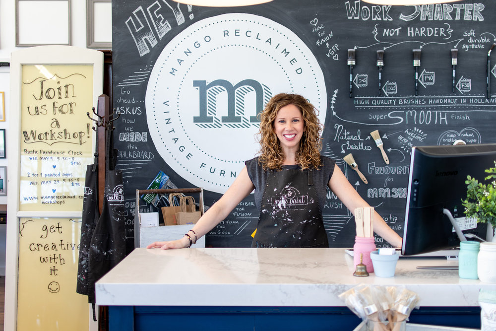 Founder of Mango Reclaimed at her front counter with fun chalkboard drawings behind her.