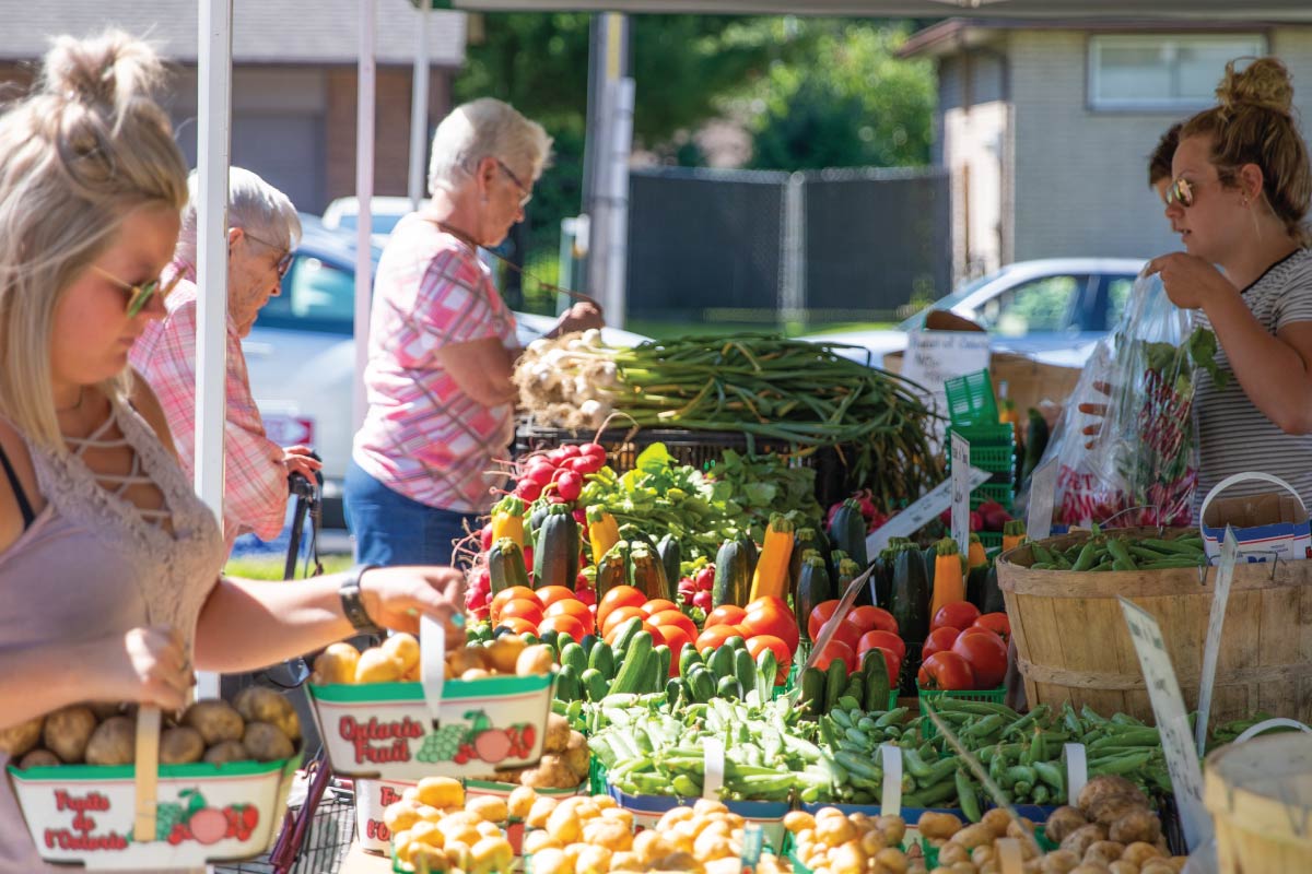 People shopping at tables full of colourful fruits and vegetables at the Clarington Farmers' Market.