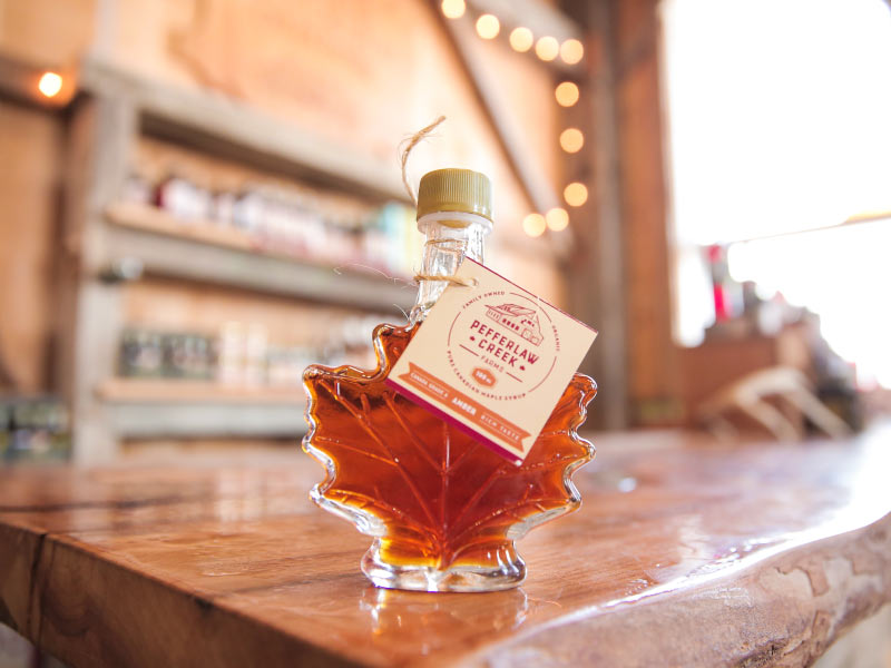 Close up of a maple leaf shaped jar or maple syrup sitting on a counter in a farm market.