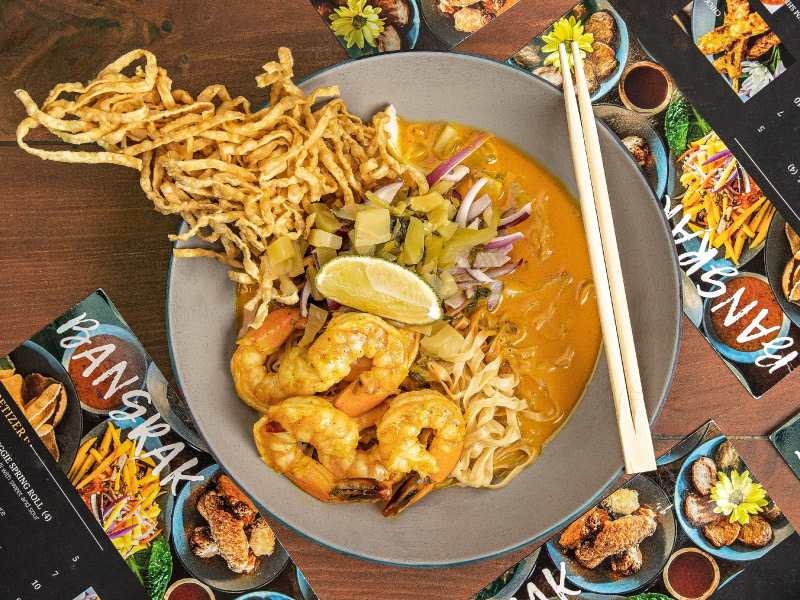 Close up of a Thai soup with shrimp, noodles, and vegetables.