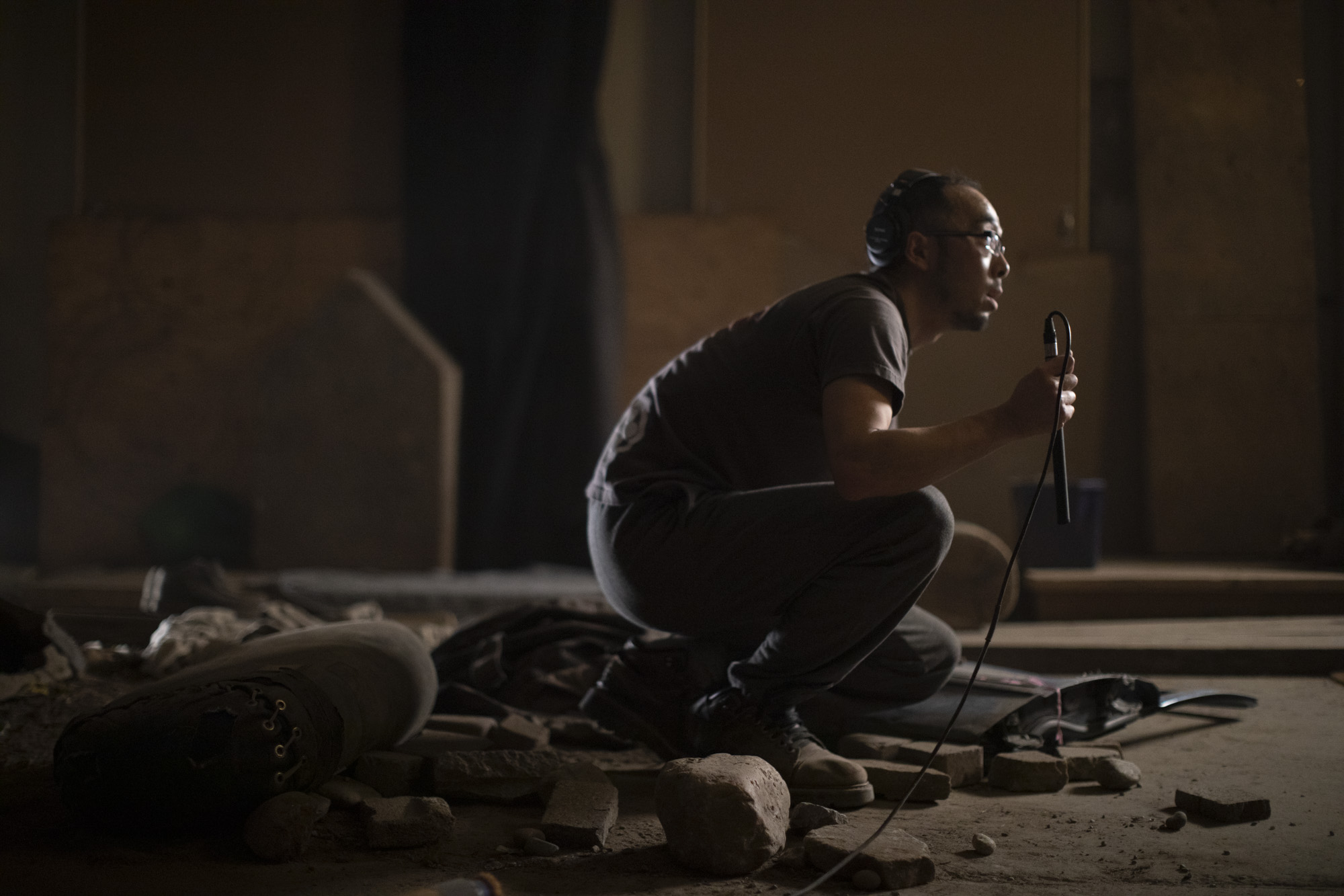 A staff member at Footsteps crouching down recording sounds with rocks and rubble near their feet.