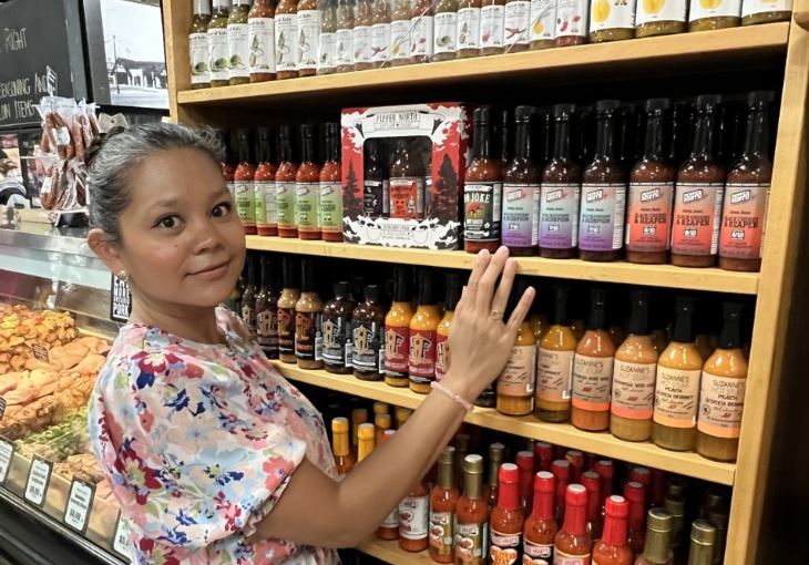 Founder of Pepper North Artisan Foods in front of her products on the shelf at a grocery store.