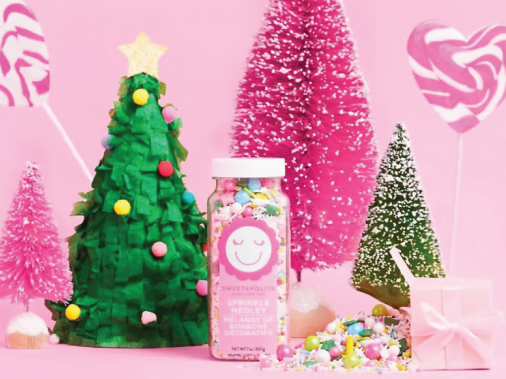 Sweetapolita Sprinkles with pink christmas trees and candy heart suckers against a pink background.