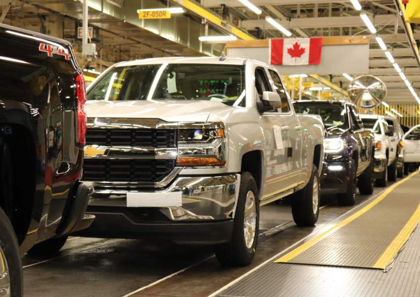 Trucks on a line inside the General Motors plant in Oshawa with a Canadian flag hanging in the background.