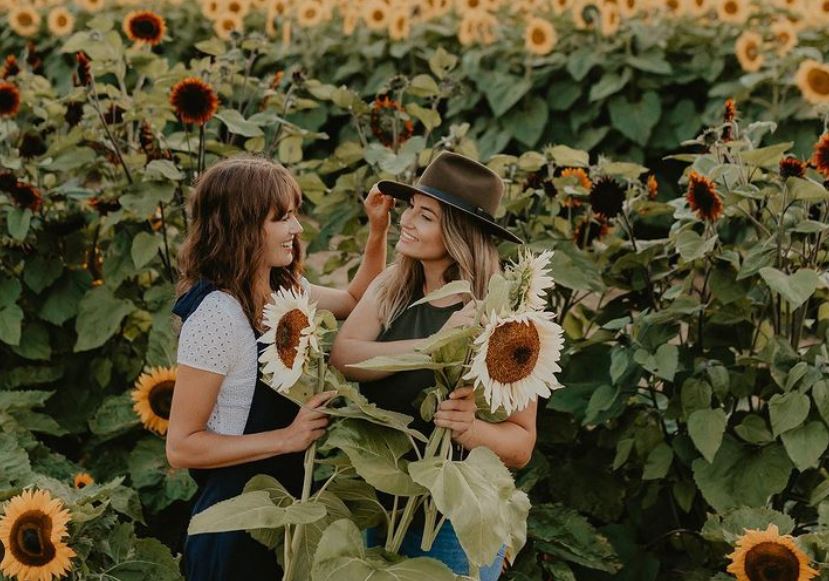 Friends holding sunflowers in a sunflower field.