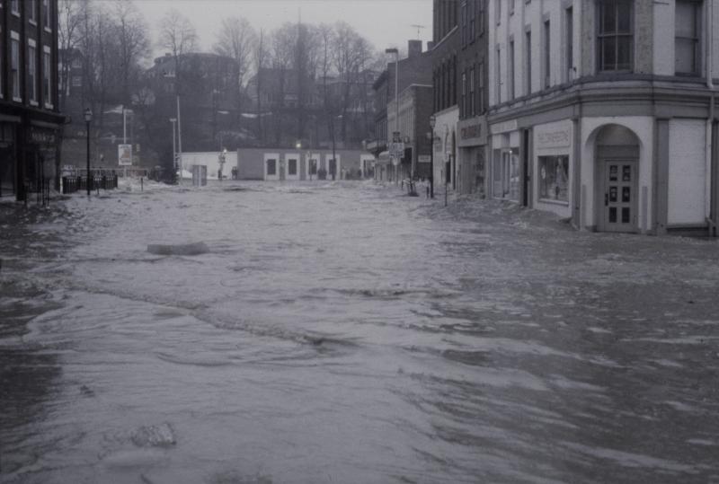 Black and white image of flooded street with closed shops and businesses