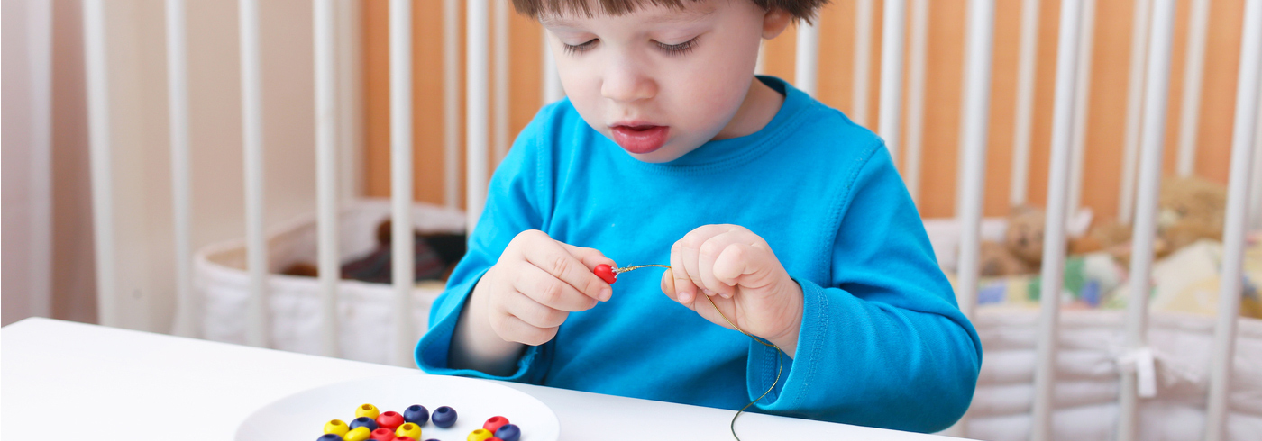 Child putting beads on a string.