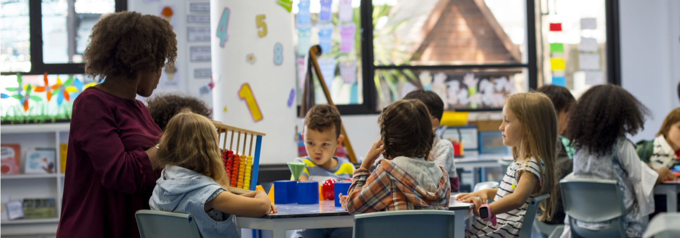 Child care employee sitting at a table with children.