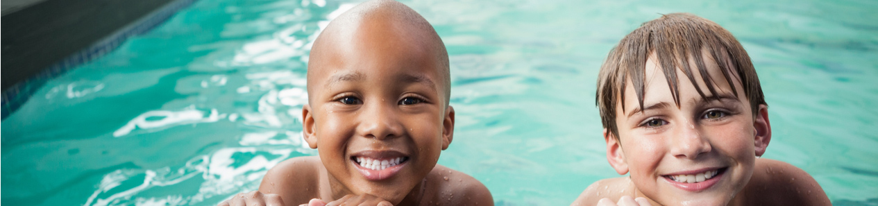 Two boys smiling at the side of a public pool