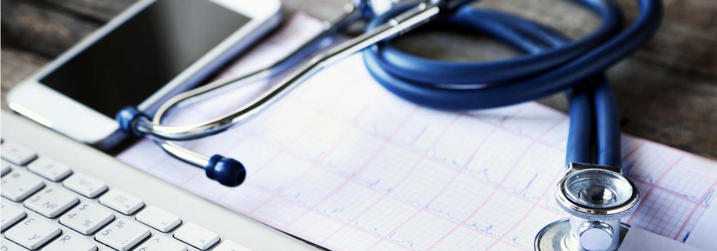 Stethoscope, report, keyboard and phone on a table.