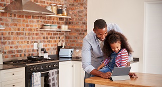 A father helps his daughter with a tablet in the kitchen