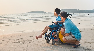 child in a wheelchair looking out over the water with an adult crouched beside him