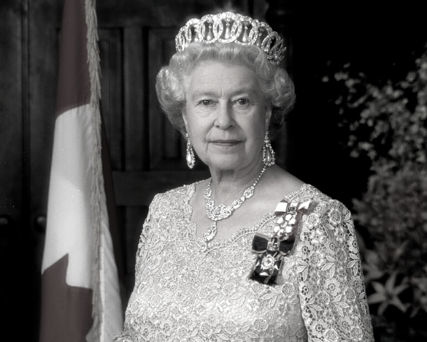 Her Majesty Queen Elizabeth II photo portrait. Wearing crown, standing in front of Canadian flag.