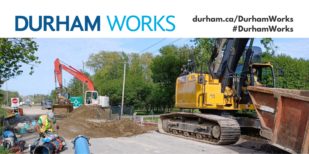 Road work with construction vehicles digging up the road, while a construction worker is at work, with a road closed sign in the background, and text above the image stating Durham Works and the website address durham.ca/DurhamWorks.