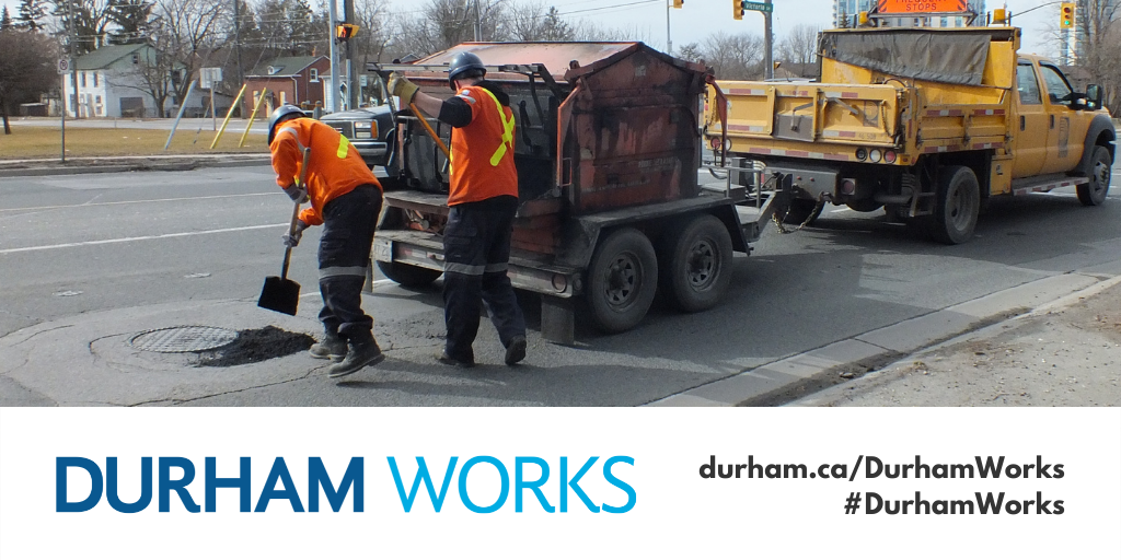 Two Regional Works Department employees fixing a pothole on a road in front of a Region truck. Text: #DurhamWorks and durham.ca/WorksBlog