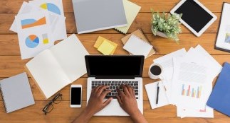 Hands typing on laptop surrounded by paperwork