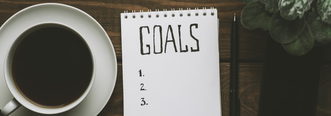 Cup of coffee on a desk, with a notepad titled goals