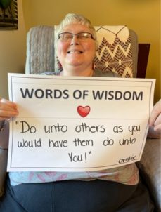 Photo of Christine holding a sign that says, "Words of Wisdom; Do unto others as you would have them do unto you!"