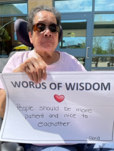 Photo of Gloria holding a sign that says, "Words of Wisdom; People should be more patient and nice to each other!"