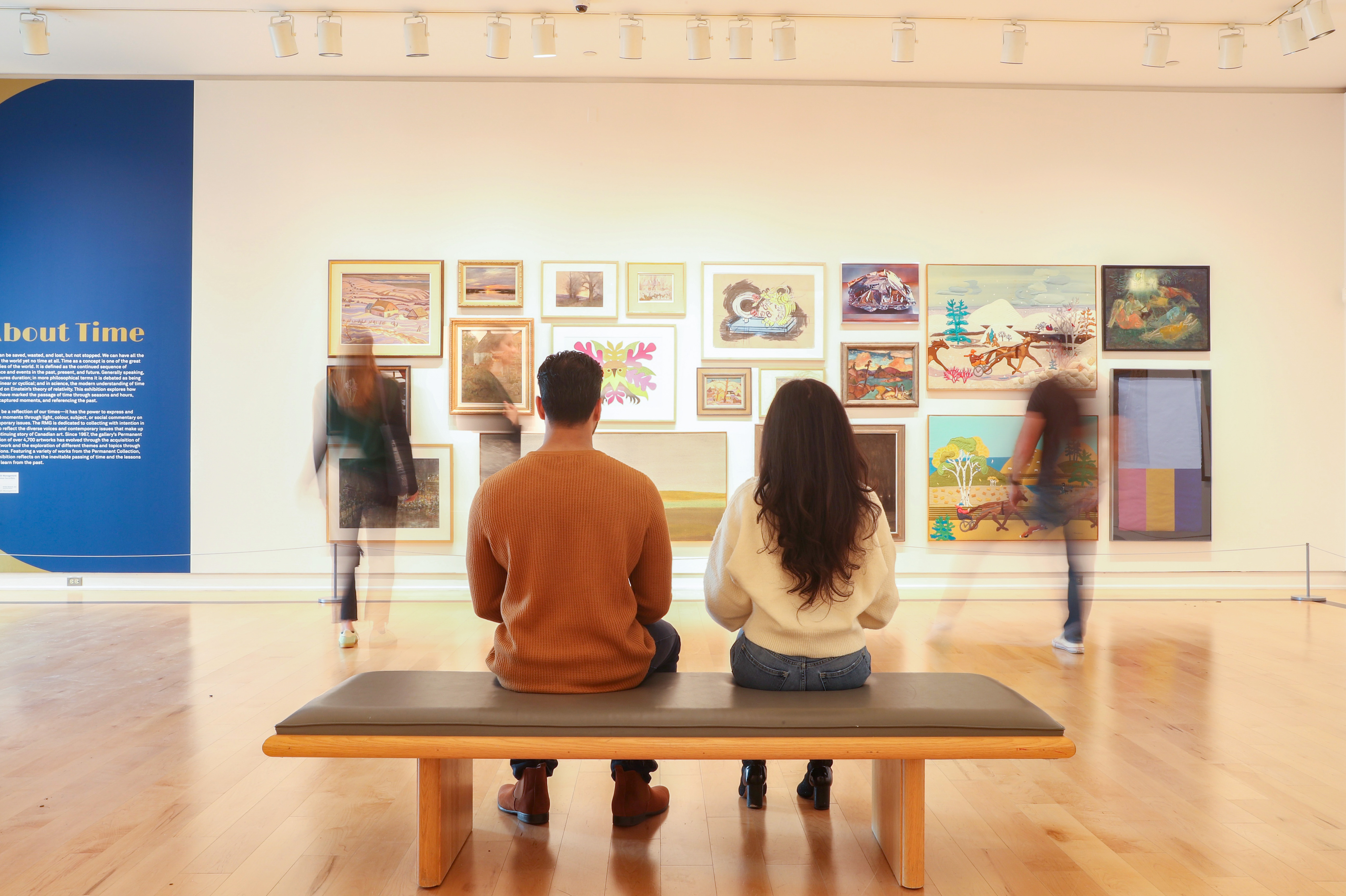 Two people sitting on a bench in a gallery.