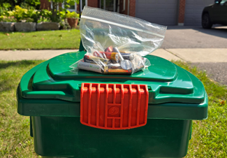 A clear bag with used batteries in it on top of a green bin. 